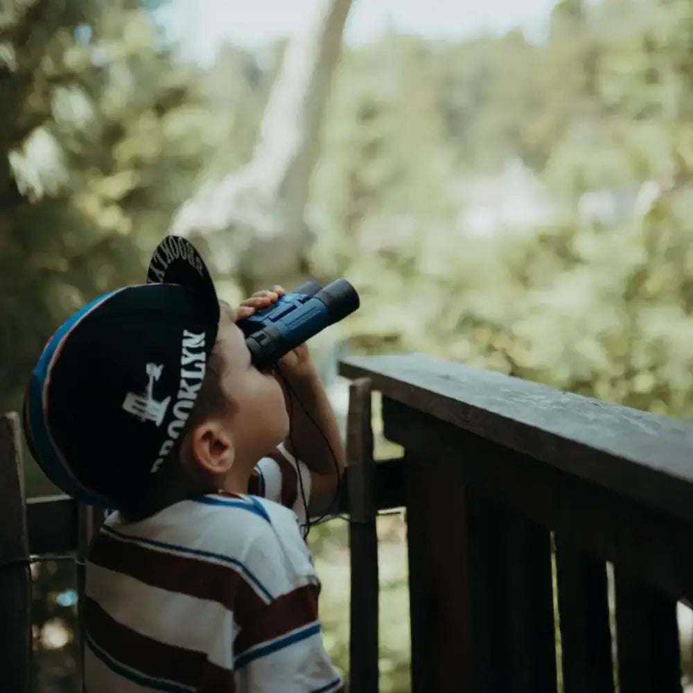 Un niño que lleva una gorra de béisbol mira a través de unos binoculares.