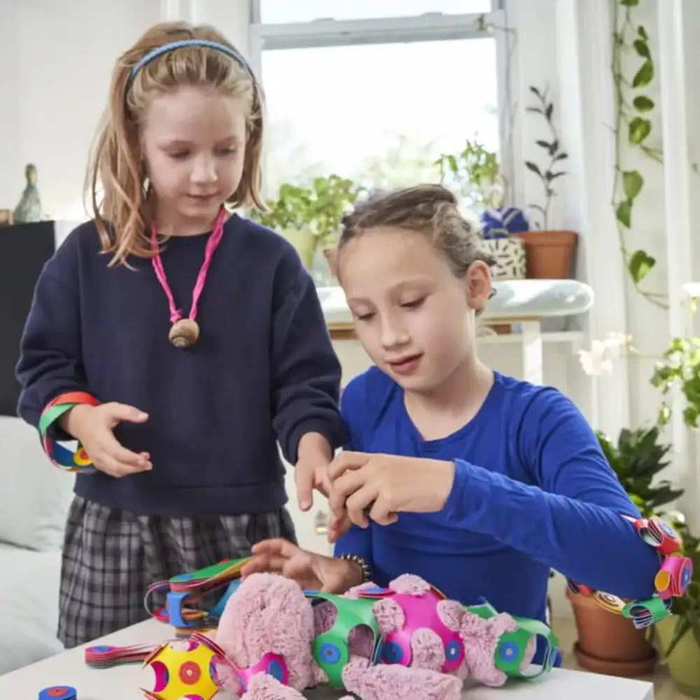 Dos niños jugando con materiales de manualidades y juguetes coloridos en una mesa.