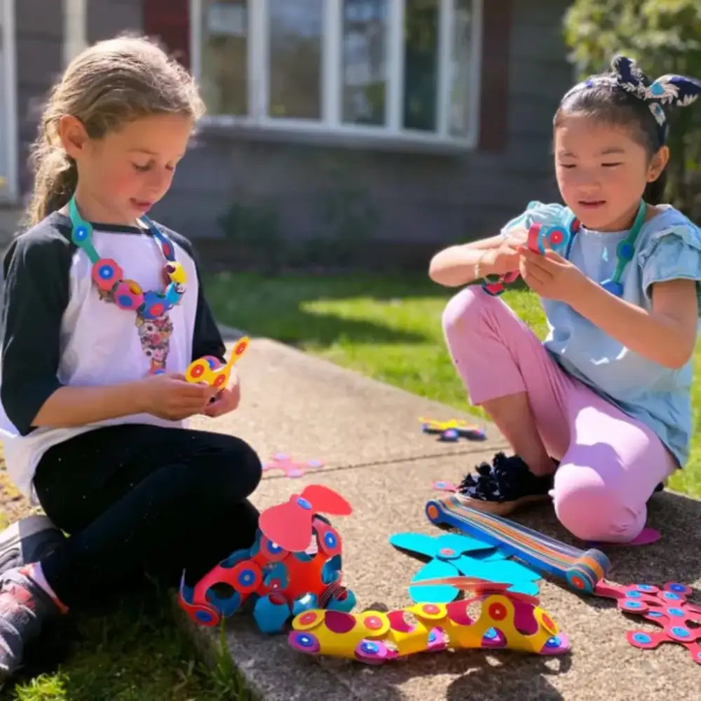 Dos niños jugando con materiales de manualidades coloridos al aire libre.